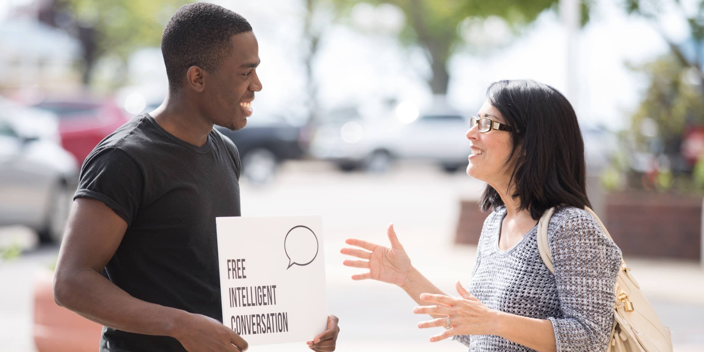 man and woman having a conversation, man is holding a "free intelligent conversation" sign