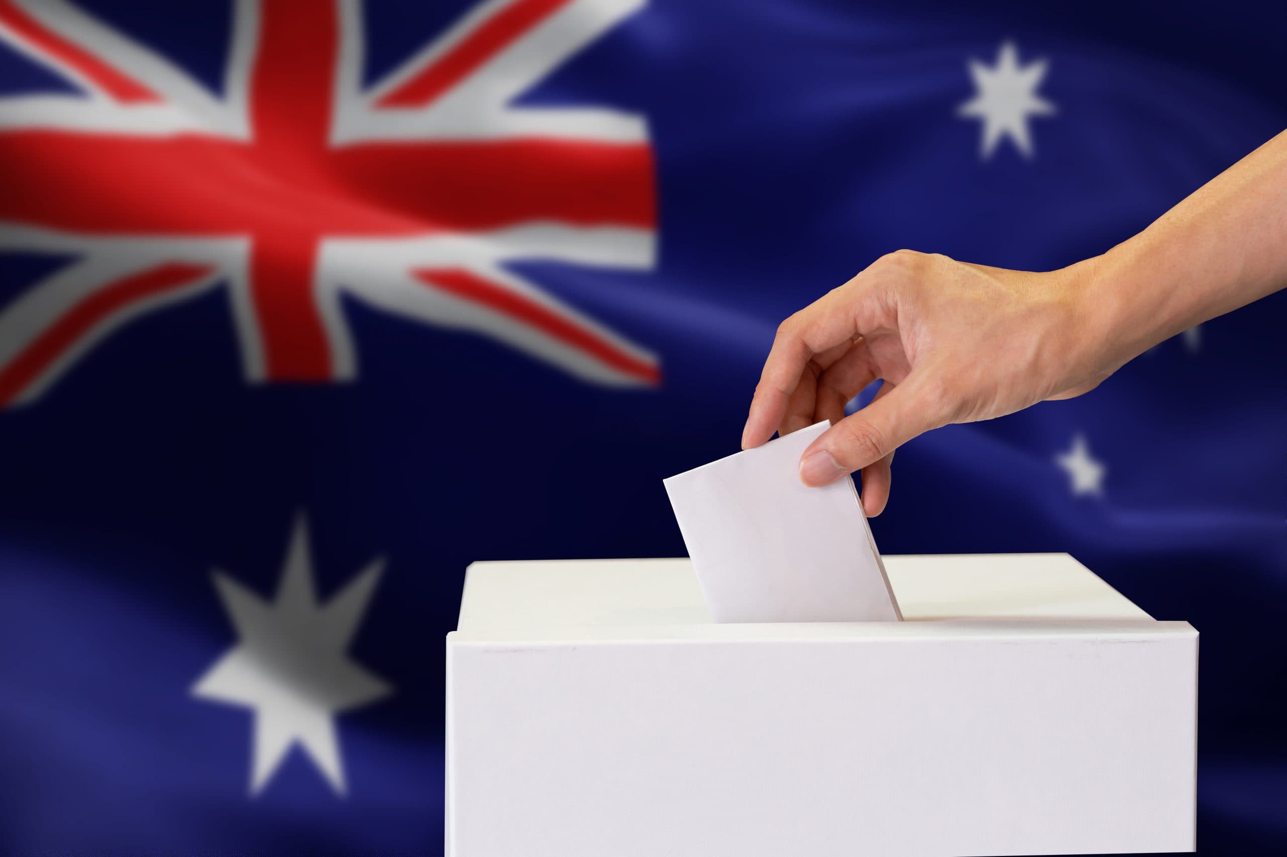 Australian Flag with ballot box in the foreground and hand putting in vote