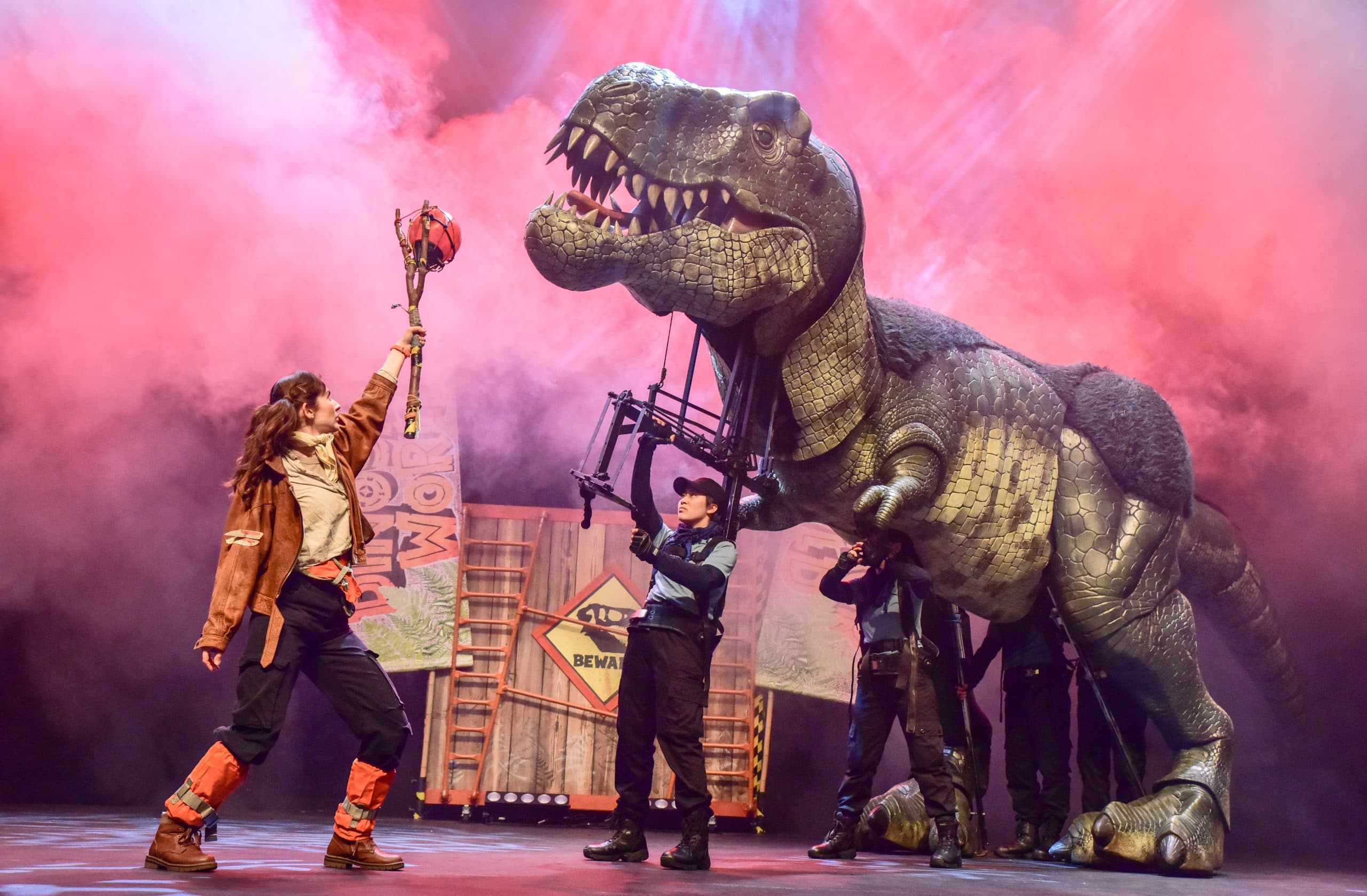 An explorer with a large-life-size dinosaur being puppetted on stage