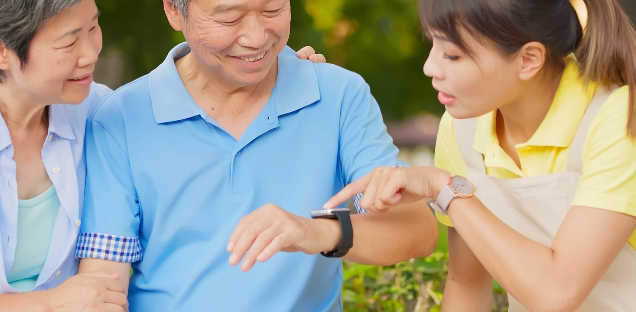 A woman is explaining a health wearable smart watch worn by an older man, watched by an older woman.