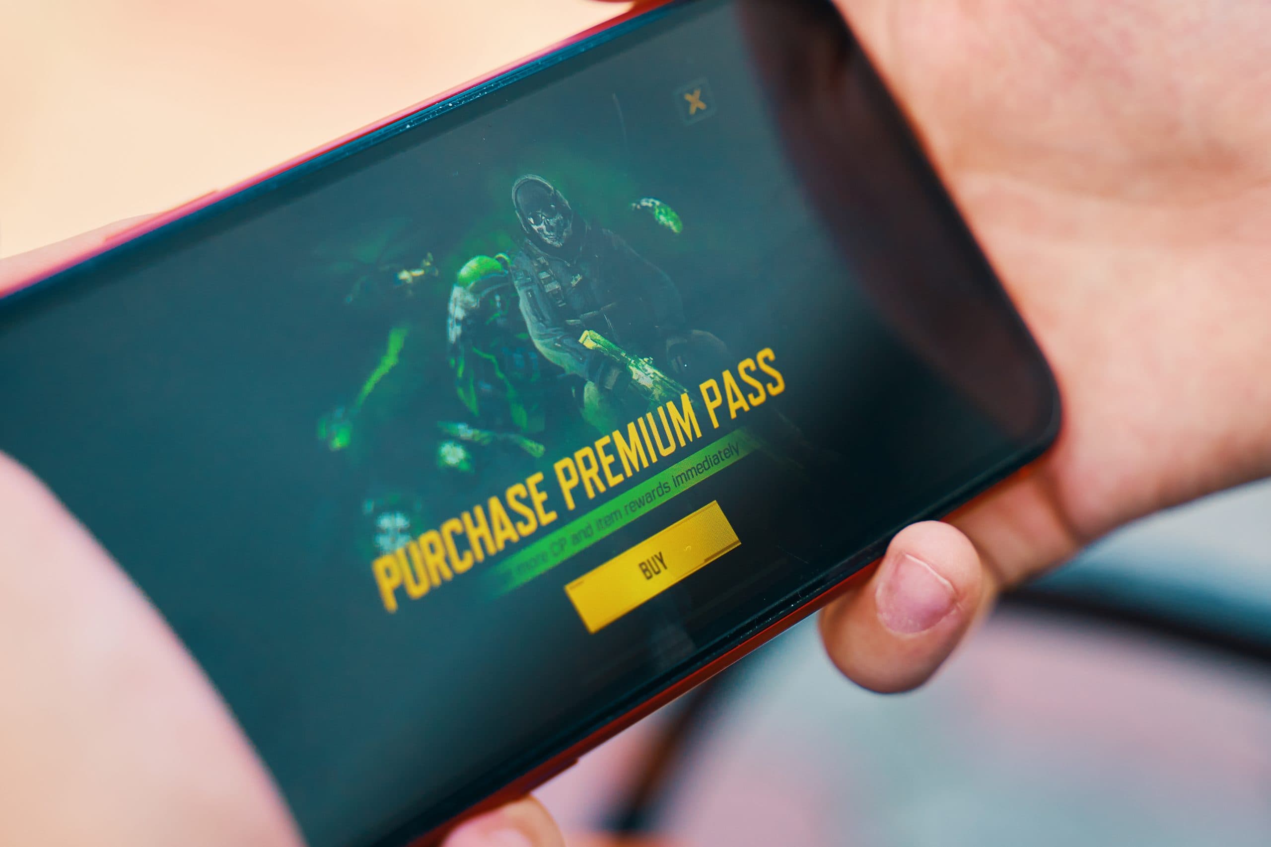 a hand holding a mobile phone with a game on it with purchase premium pass written on the screen in bold yellow text