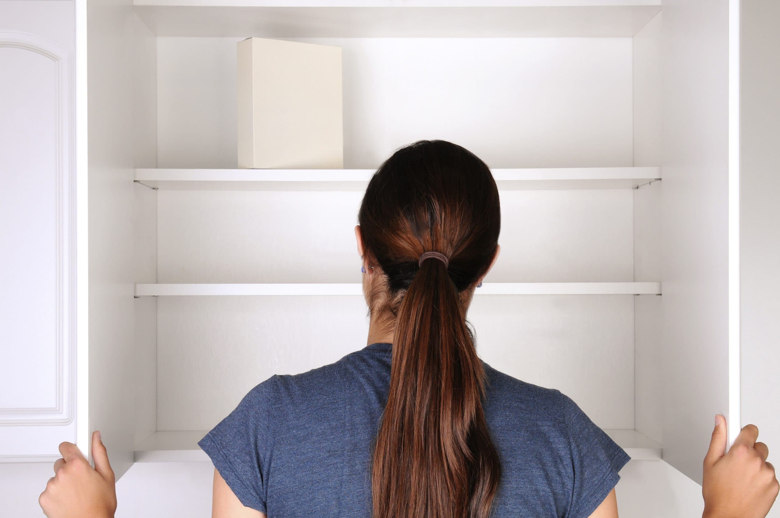 image of a woman looking at an empty cupboard, with only one packet in the back of the cupboard