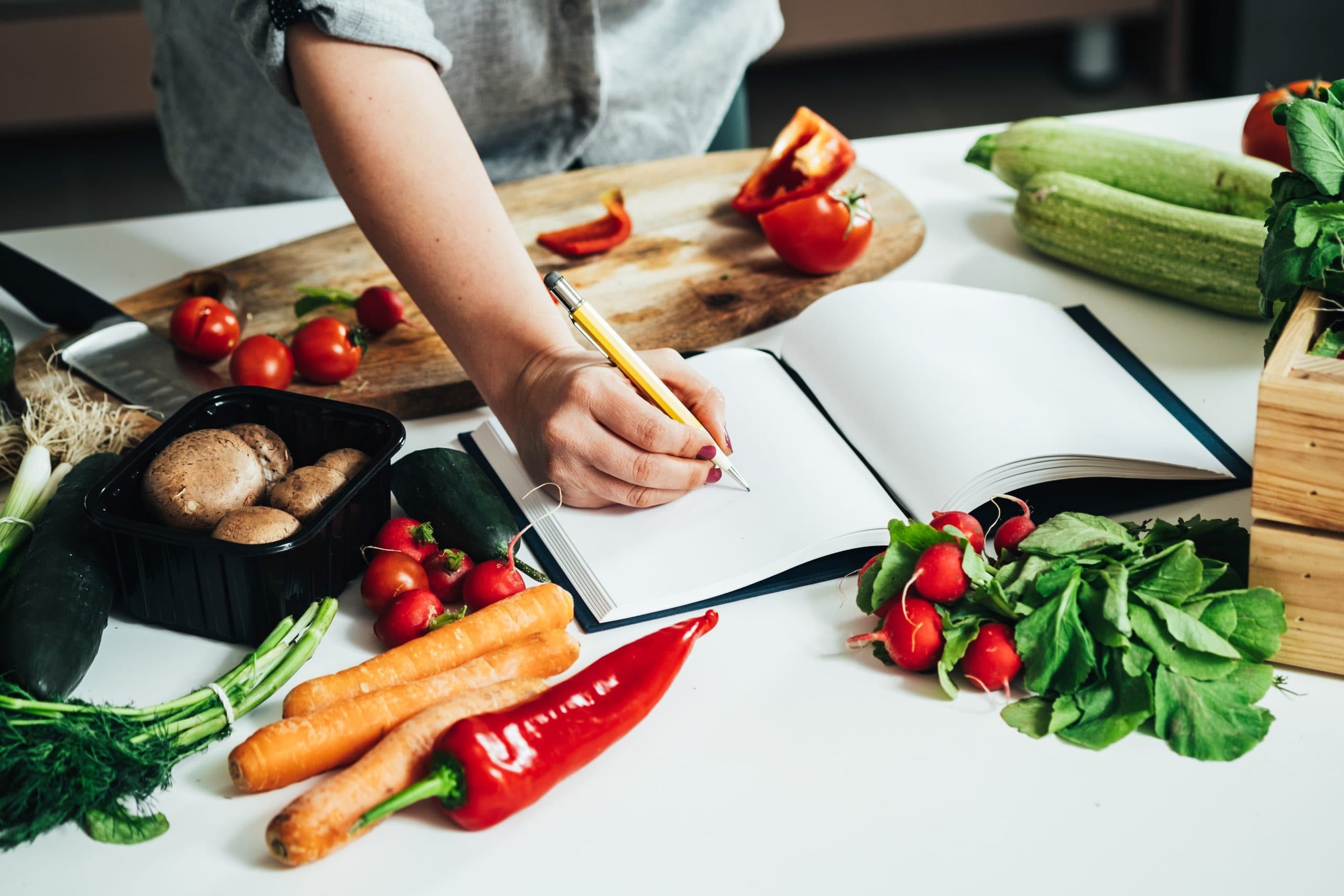an image of a woman writing in a blank book surrounded by a variety of vegetables