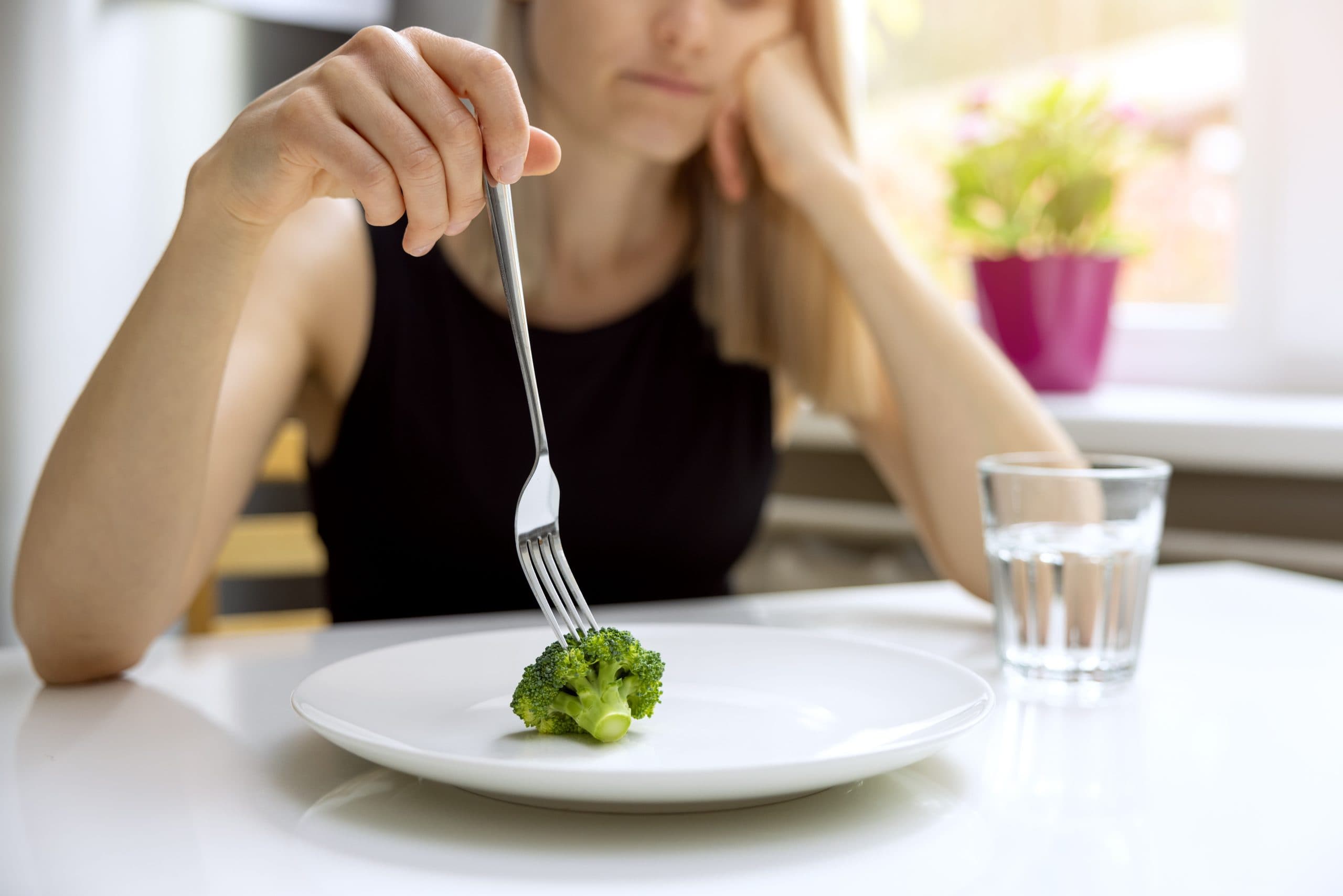 an image of a young woman placing a fork into a single broccoli, appearing dejected