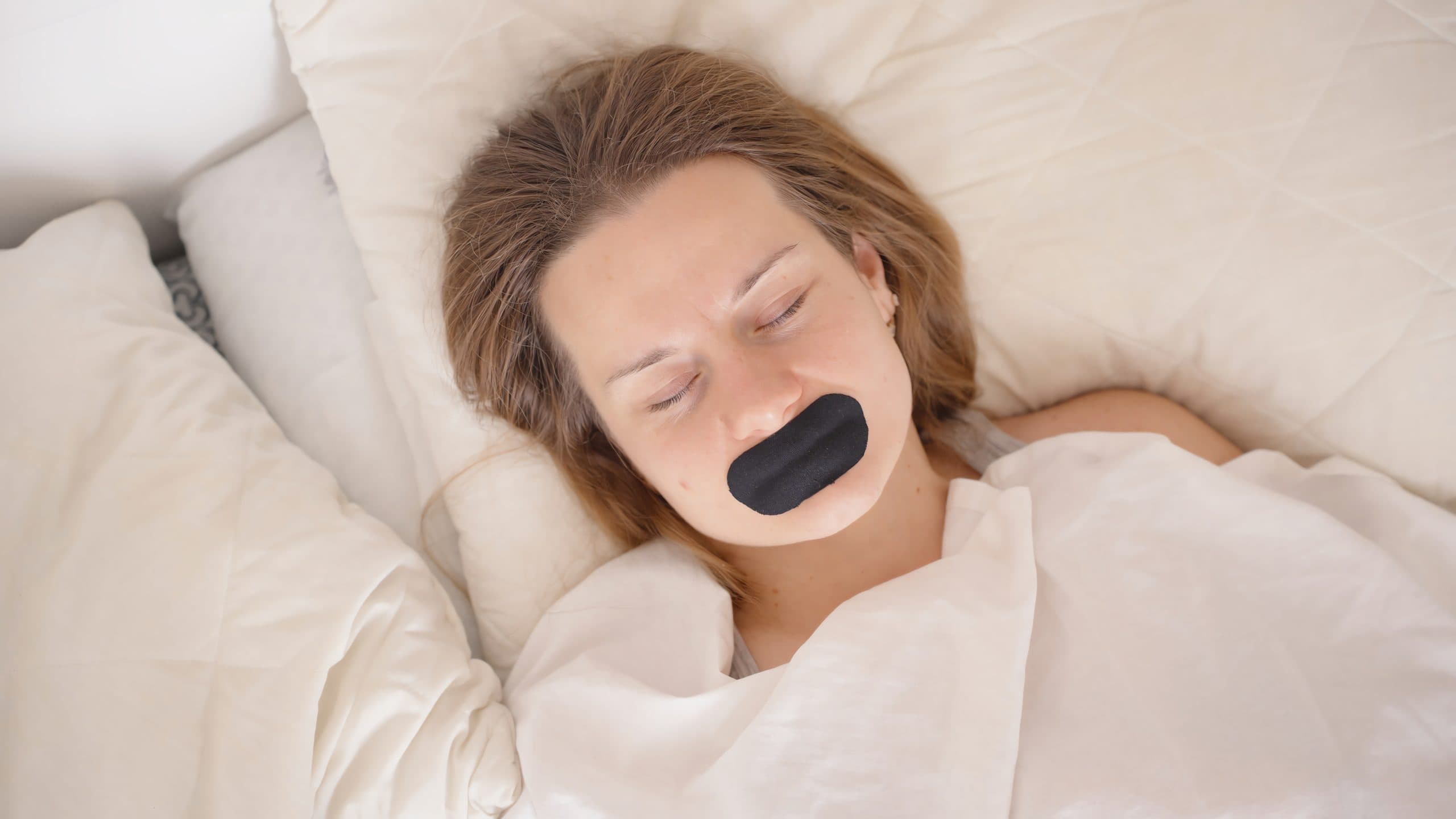 a woman lying on her back in a bed with black tape over her mouth