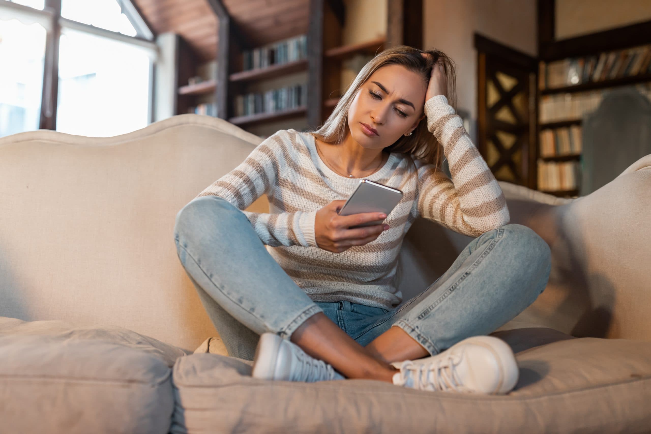 a woman looking at her phone with her legs crossed and a distressed expression