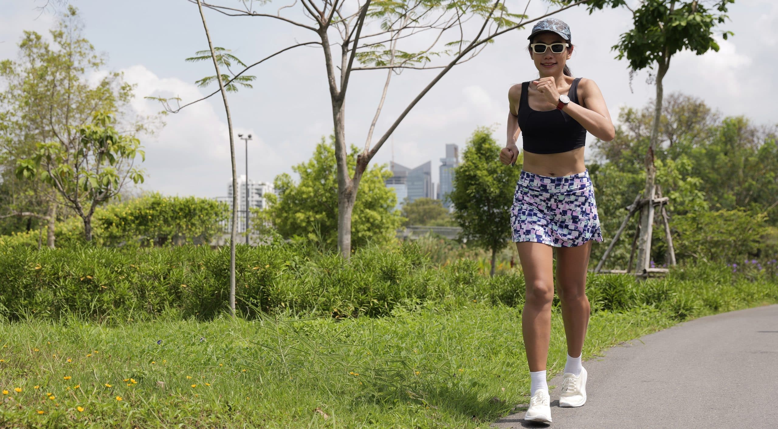 a young, athletic looking woman running across a concrete path wearing a black tank top and skorts